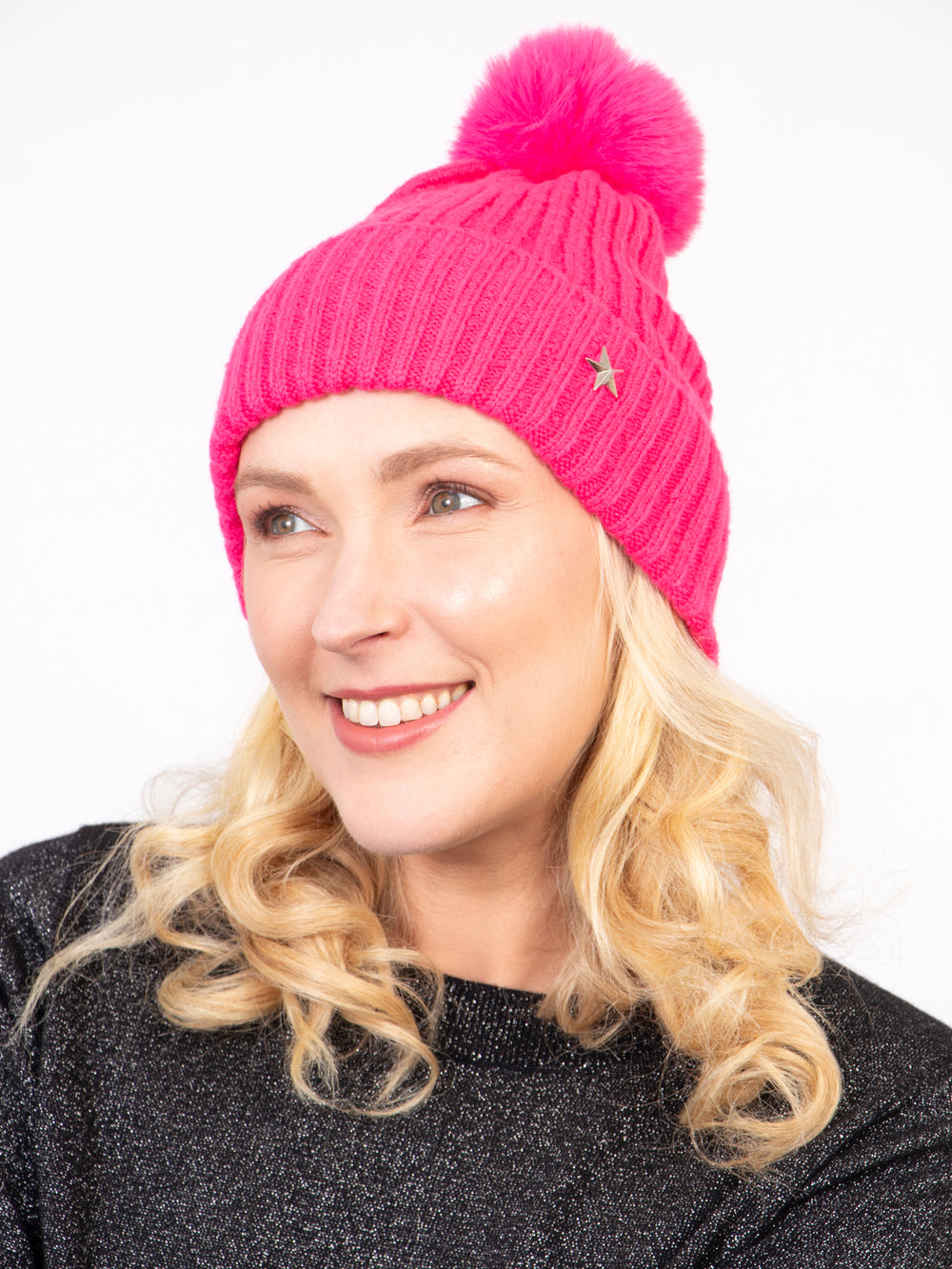 model wearing a fuchsia pink coloured knitted ribbed beanie hat with a pom pom on top and a gold metallic star on the brim.