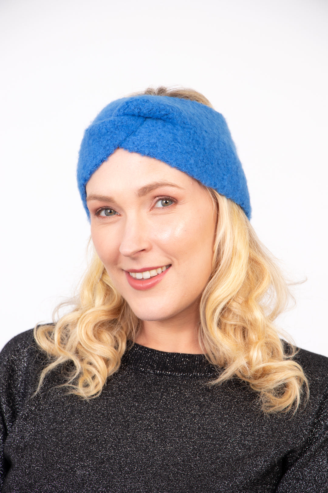 model wearing a royal blue knitted twist front headband, the band covers the ears and forehead