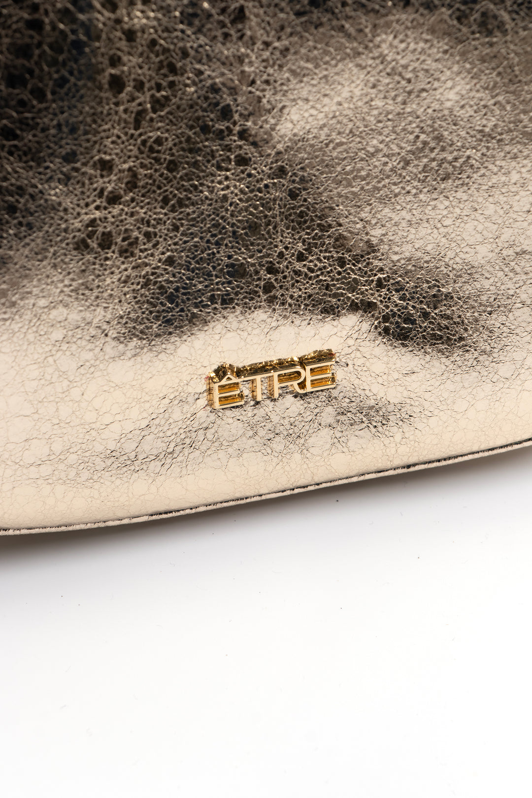 close up of the cracked faux leather and the gold etre logo on the front of the bag