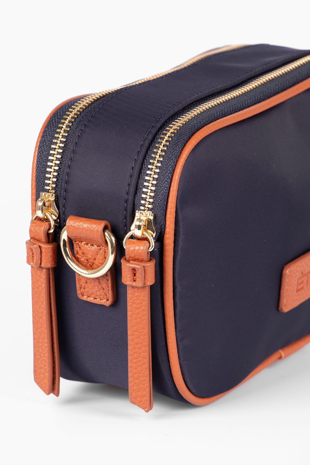 close up of the end of the bag, showing clearly the twin zip fastening compartments, There are two gold zips on the top of the bag each with tan faux leather tabs