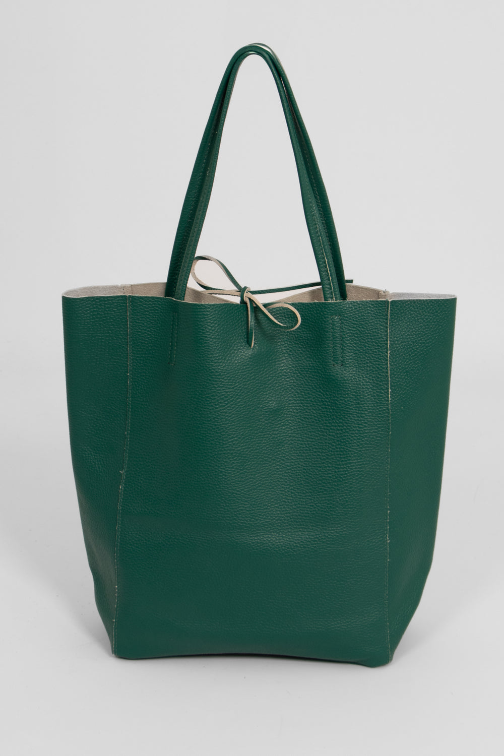 emerald green leather tote bag standing upright. the top tie fastening is  in the centre of the top of the bag. the handles are thin.