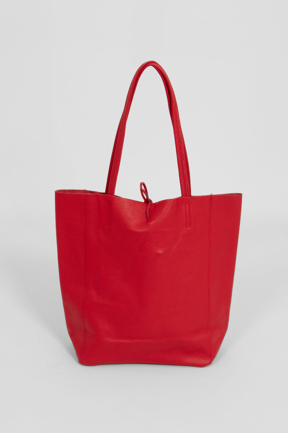 the red leather tote bag is standing upright, this images shows the back of the bag which is plain red.