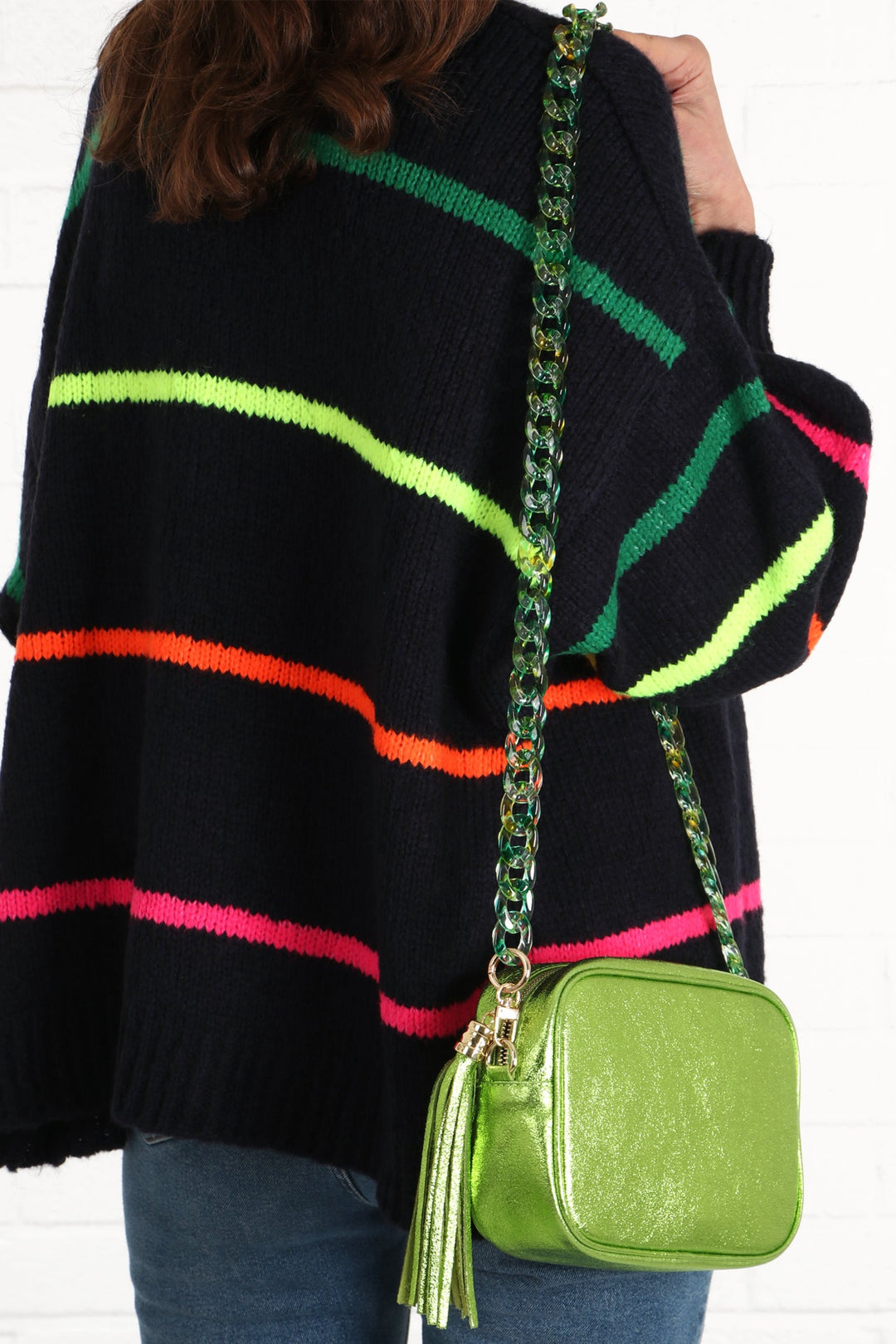 model wearing a metallic green camera bag with acrylic green bag strap and a multicoloured stiped cardigan