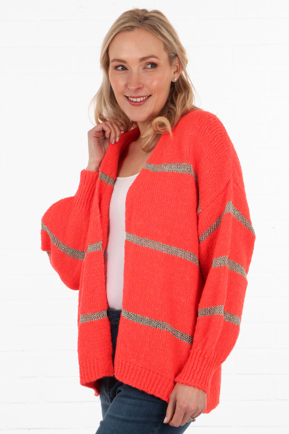 model showing the side view of the coral pink and gold striped cardigan, stiped are horizontal on the front and on the sleeves