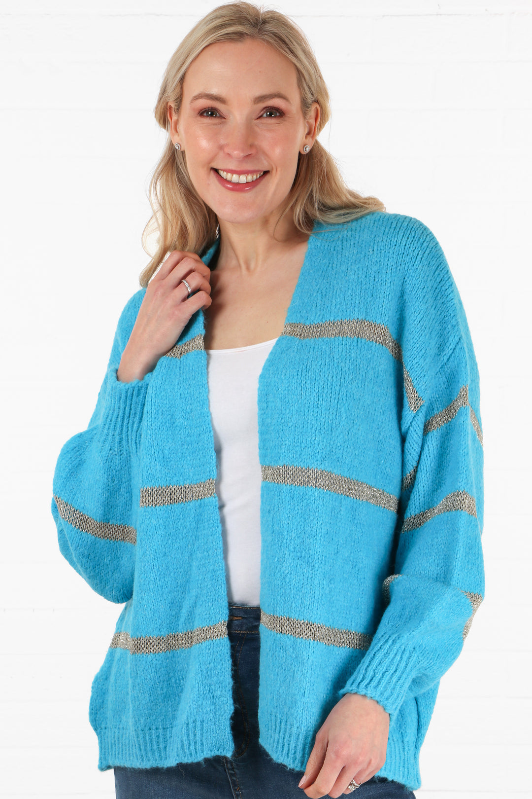 model wearing a blue open front cardigan with a horizontal knitted gold glitter stripe throughout