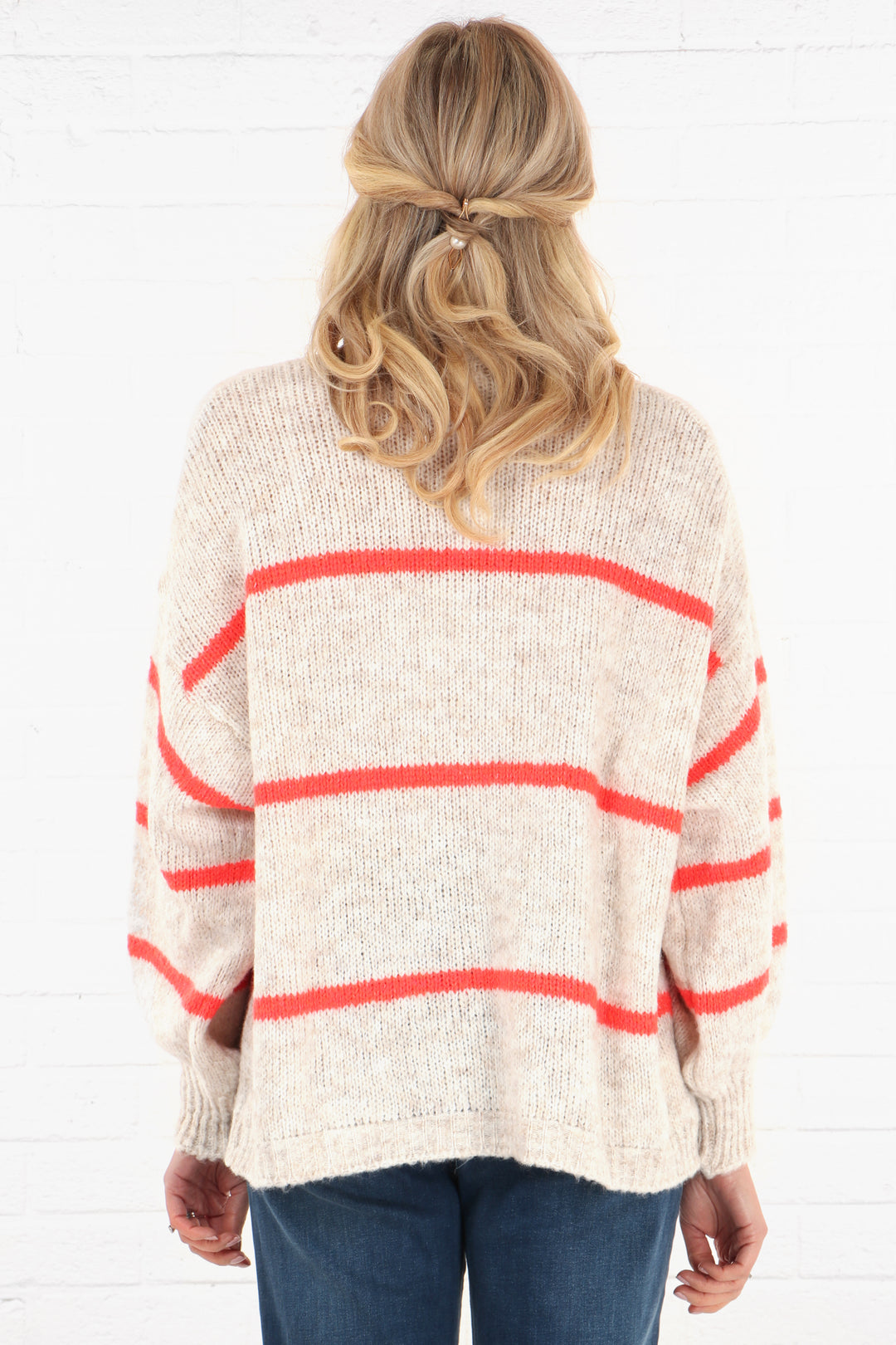 model showing the back of the cream knitted cardigan, showing the contrasting thin coral stripes 