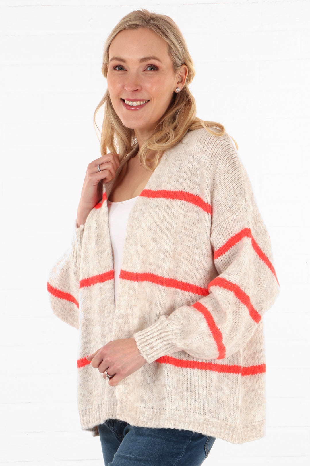 model showing a side view of the cream cardigan, showing that the coral stripes are also on the sleeves