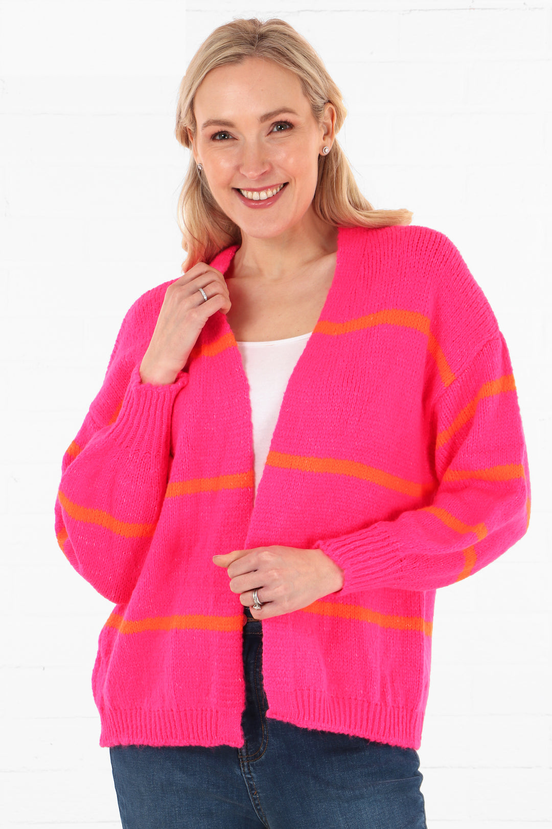 model wearing a pink open front cardigan with three orange horizontal stripes