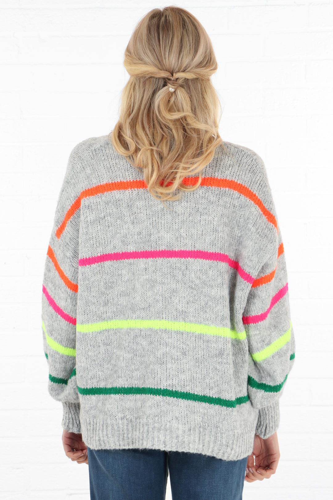 model showing the back of the grey cardigan with a multicoloured stripe pattern, stripes are green, yellow, pink and orange