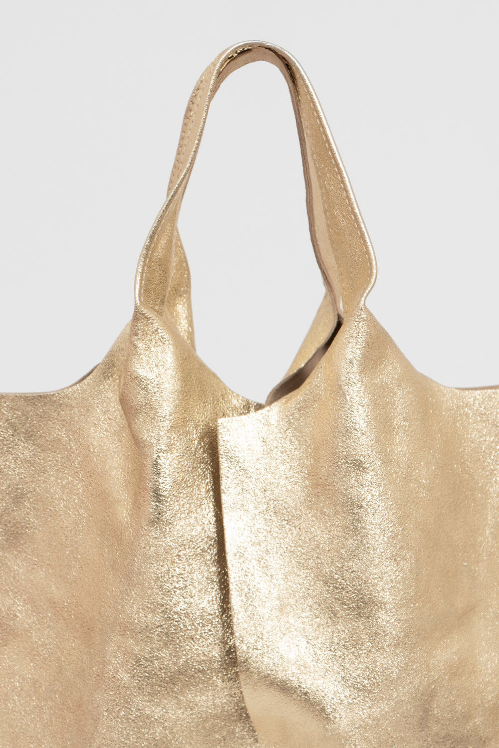 close up of the metallic gold leather and the carry handle on the top of the bag