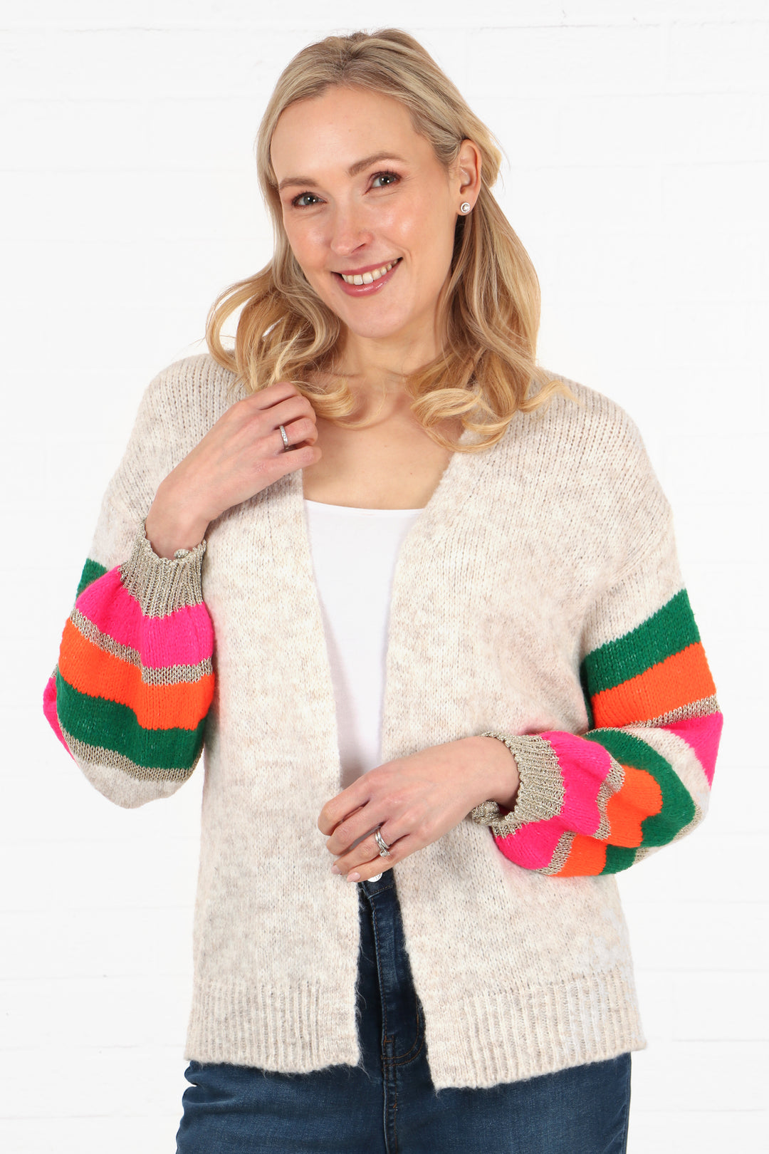 model wearing a cream knit open front short cardigan with colourful striped sleeves. Sleeves are green, pink, orange and gold glitter striped