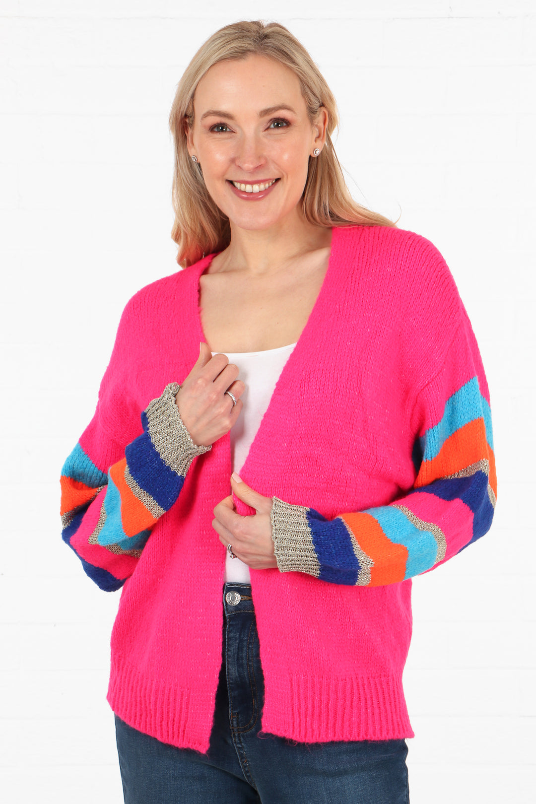 model wearing a fuchsia pink open front cardigan with multicoloured striped sleeves, the sleeves are light blue, dark blue, orange and gold glitter striped