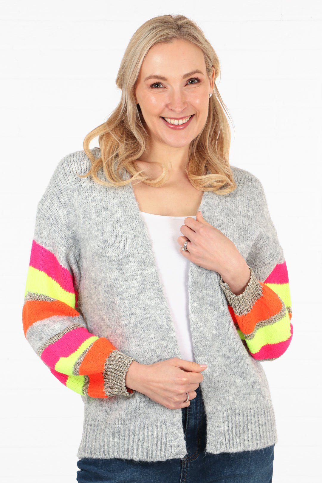 model wearing a grey open front knit cardigan with multicoloured striped sleeves. sleeves are pink, orange, neon yellow and gold glitter striped