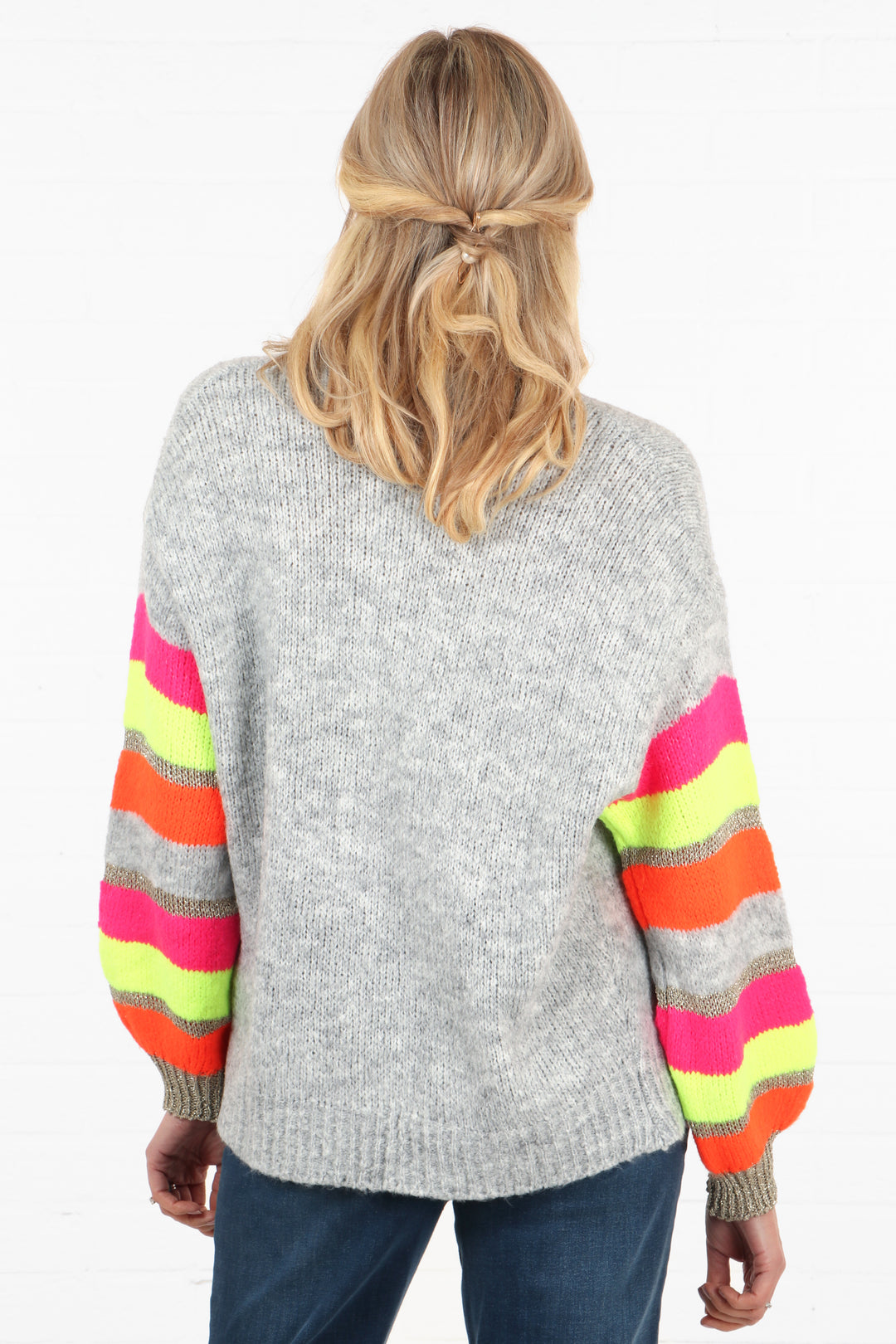 model showing the back of the cardigan which is light grey, the sleeves are multicoloured stiped