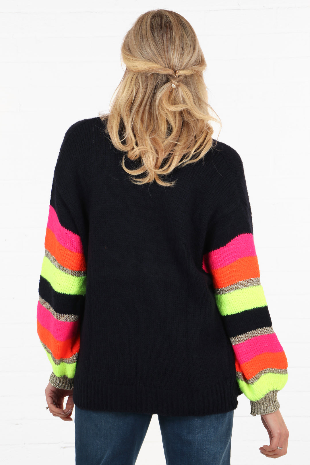 model showing the back of the cardigan, showing that the back is solid navy blue while the sleeves are colourfully stripes in pink, orange, neon yellow and gold