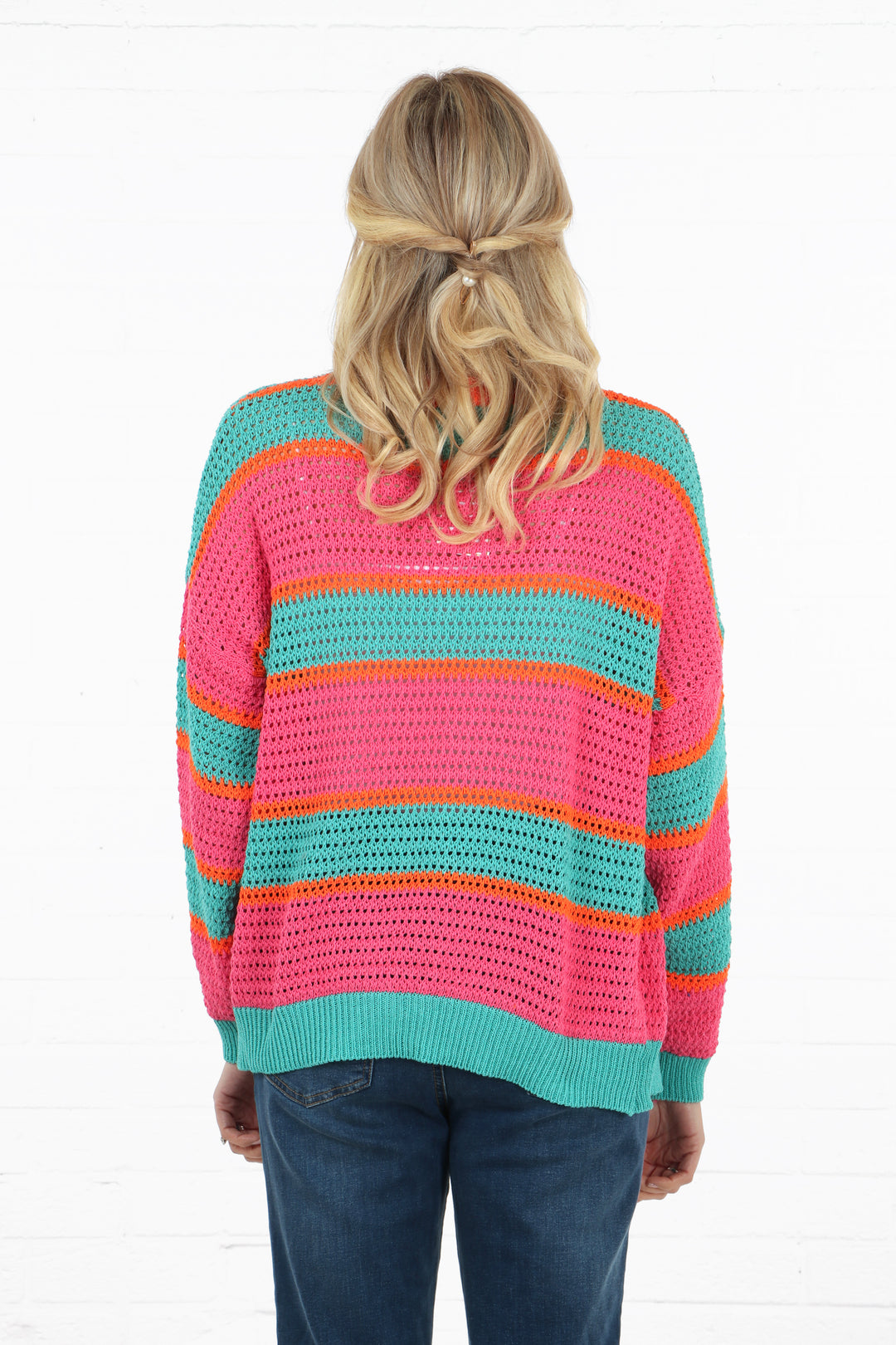 model showing the back of the stiped cardigan, showing the open knit material and pink, orange and turquoise striped pattern