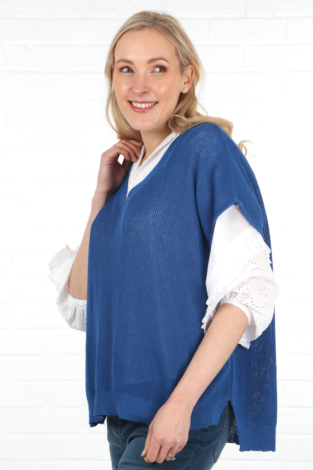 model showing the side view of the blue cotton knitted tank top sleeveless jumper, showing a dip hem with the hem being slightly longer at the back than at the front