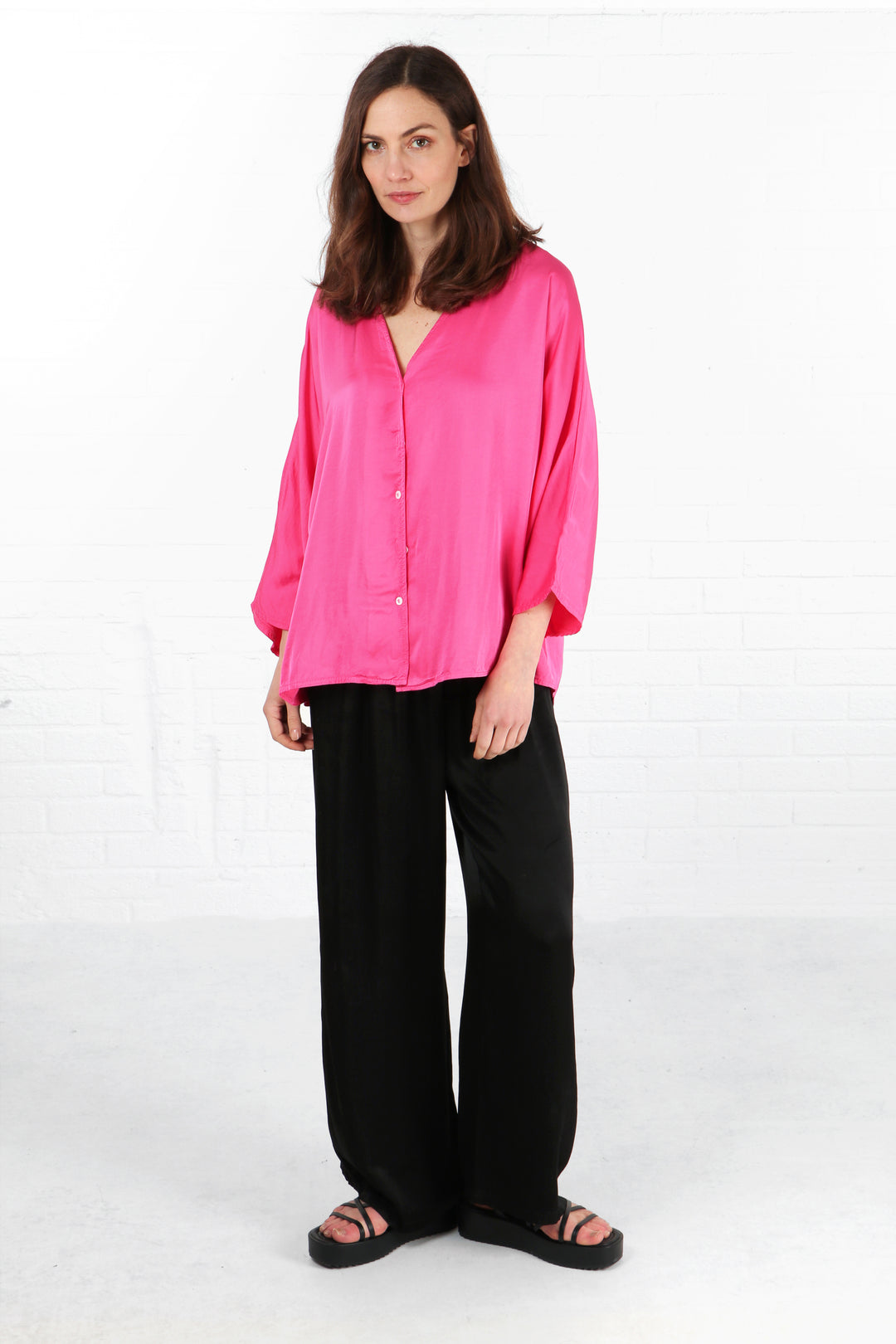 model wearing a silky textured 3/4 sleeve v neck pink blouse with a button down front