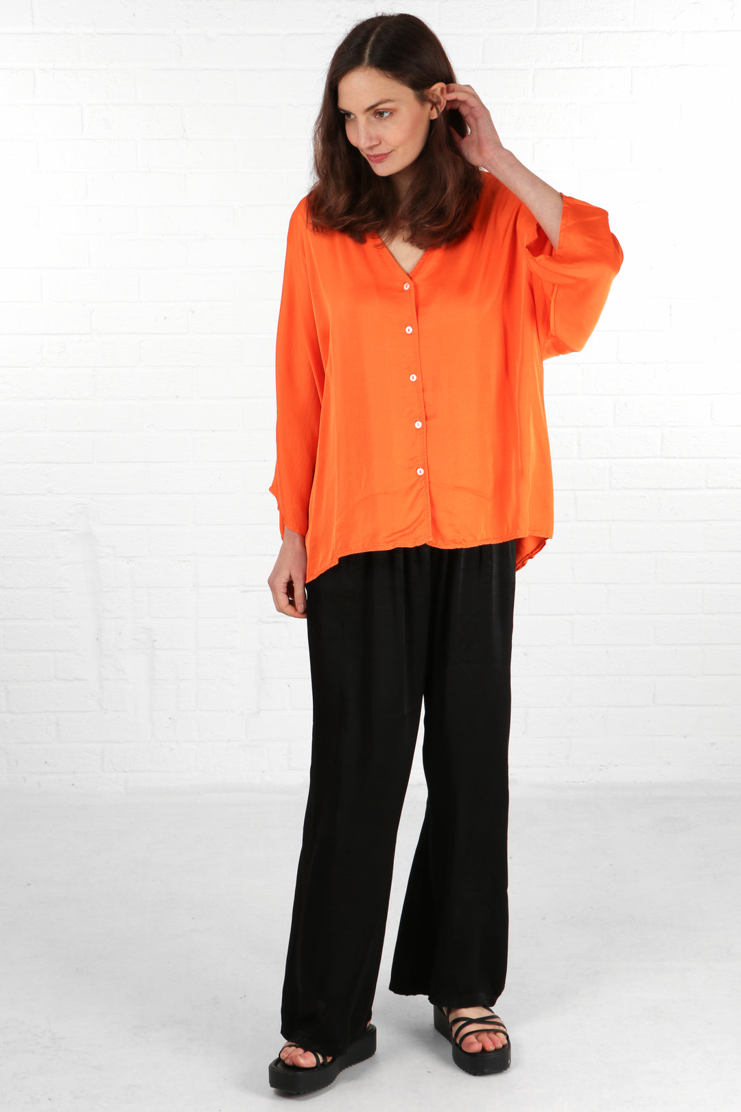 model wearing a loose fitting orange silky textured blouse