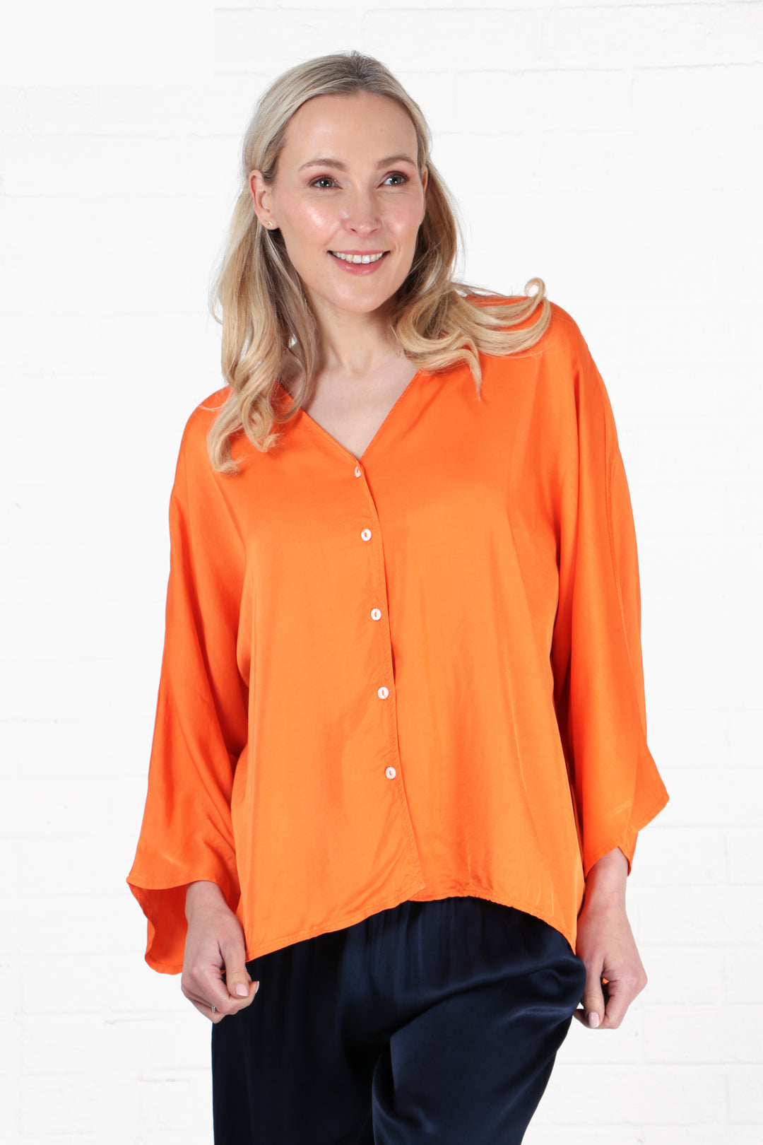 model wearing an orange button down blouse with a collarless v neck and 3/4 sleeves