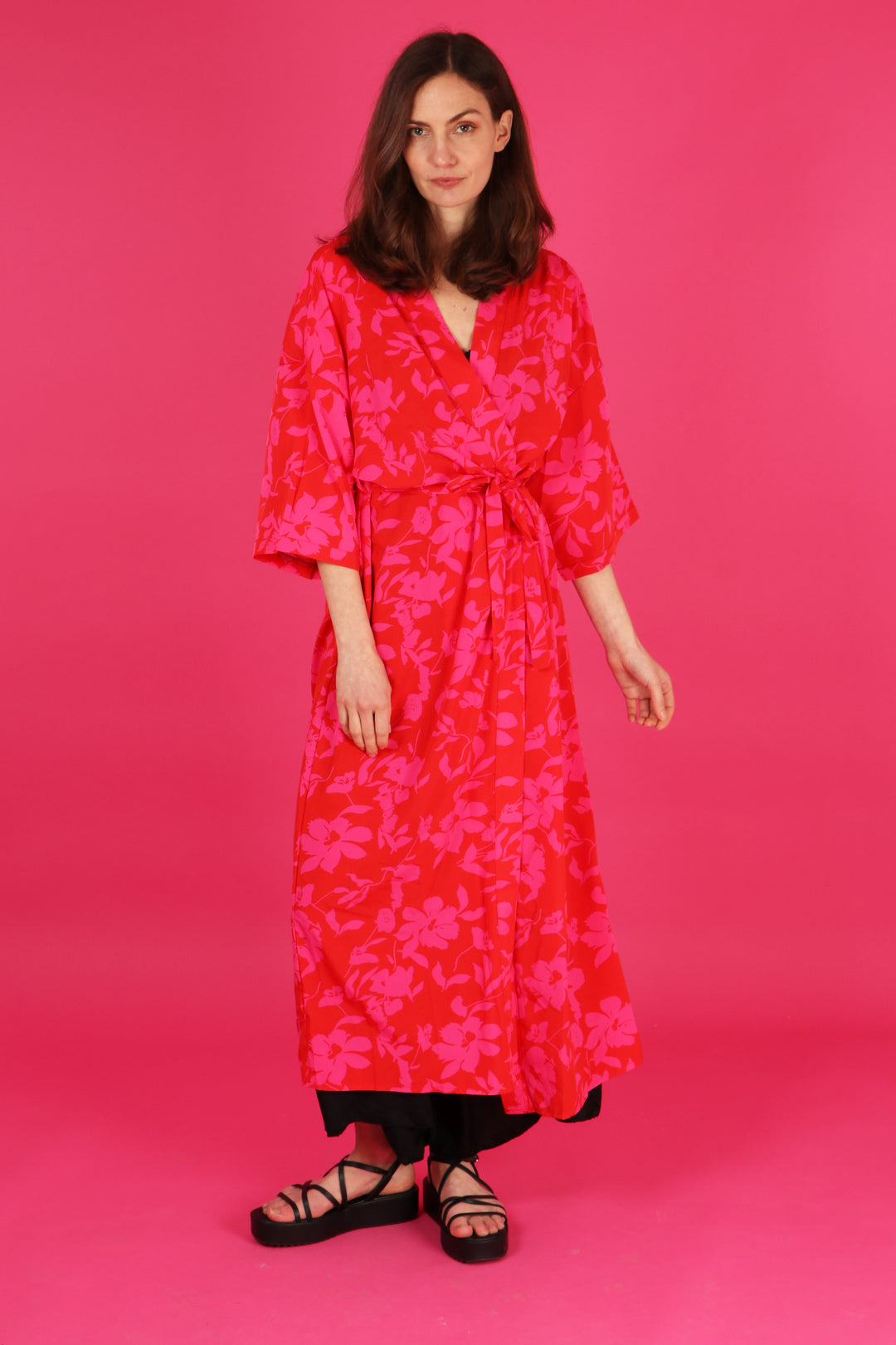 model wearing a red and pink floral long kimono robe with 3/4 sleeves and waist tie