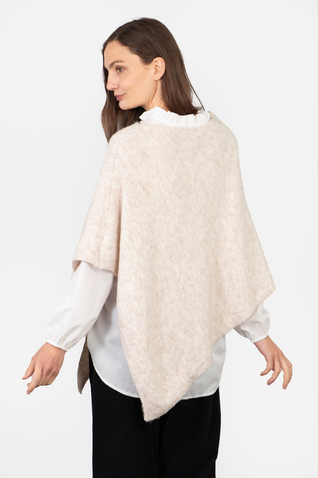 model showing the back of the cream poncho, highlighting the asymmetrical hem and plain pattern