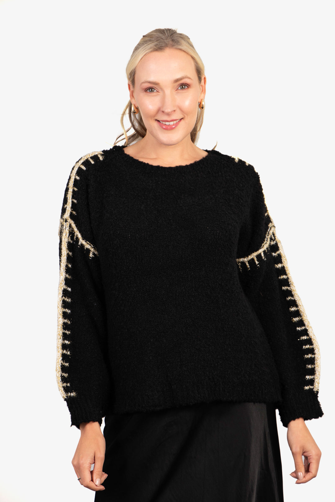 model wearing a black long sleeve knitted jumper, the jumper has bold gold glitter stitch pattern on the entire length of the sleeves