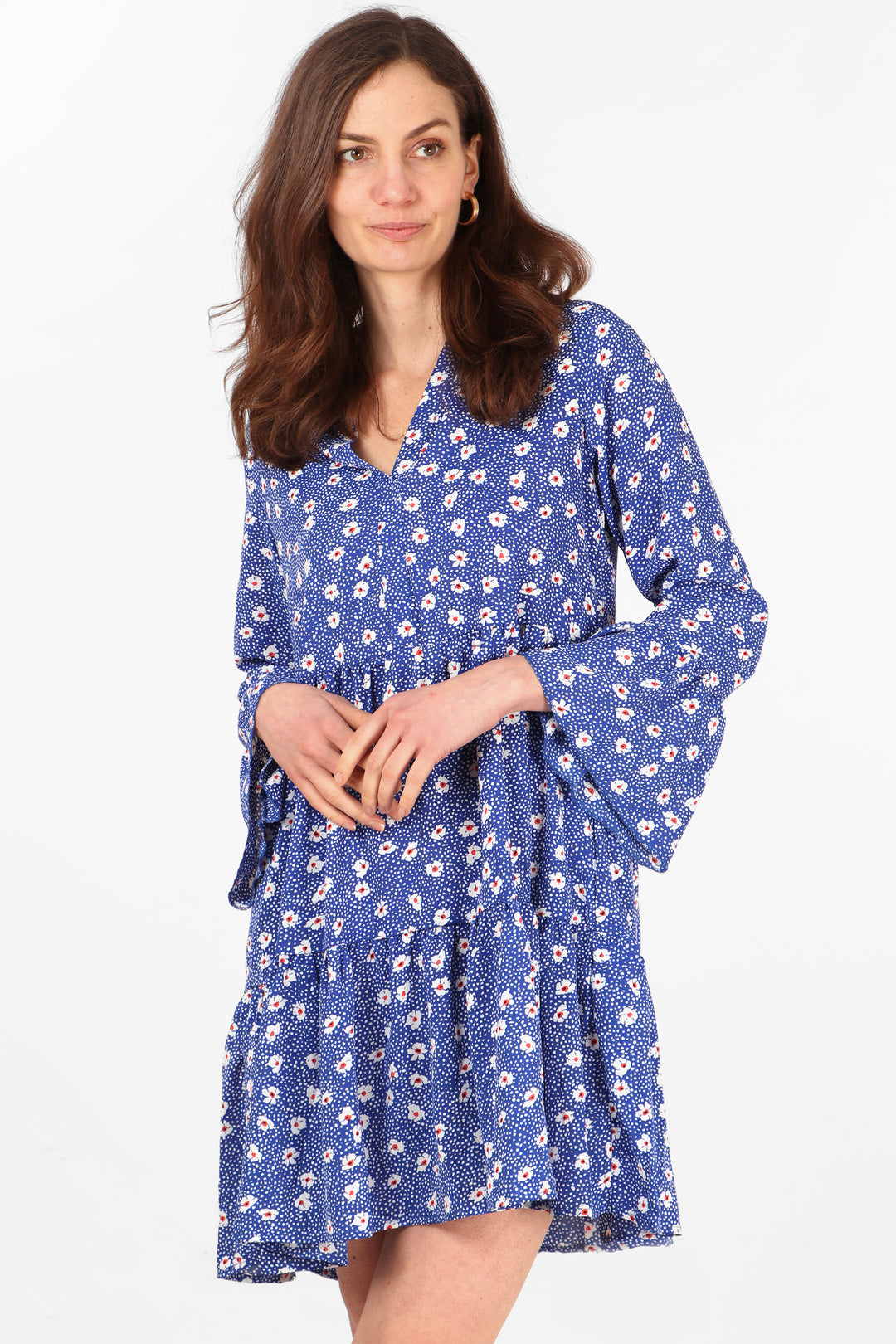 model wearing a blue tiered mini dress with an all over daisy floral and spot print pattern, the dress has v neck and long fluted sleeves