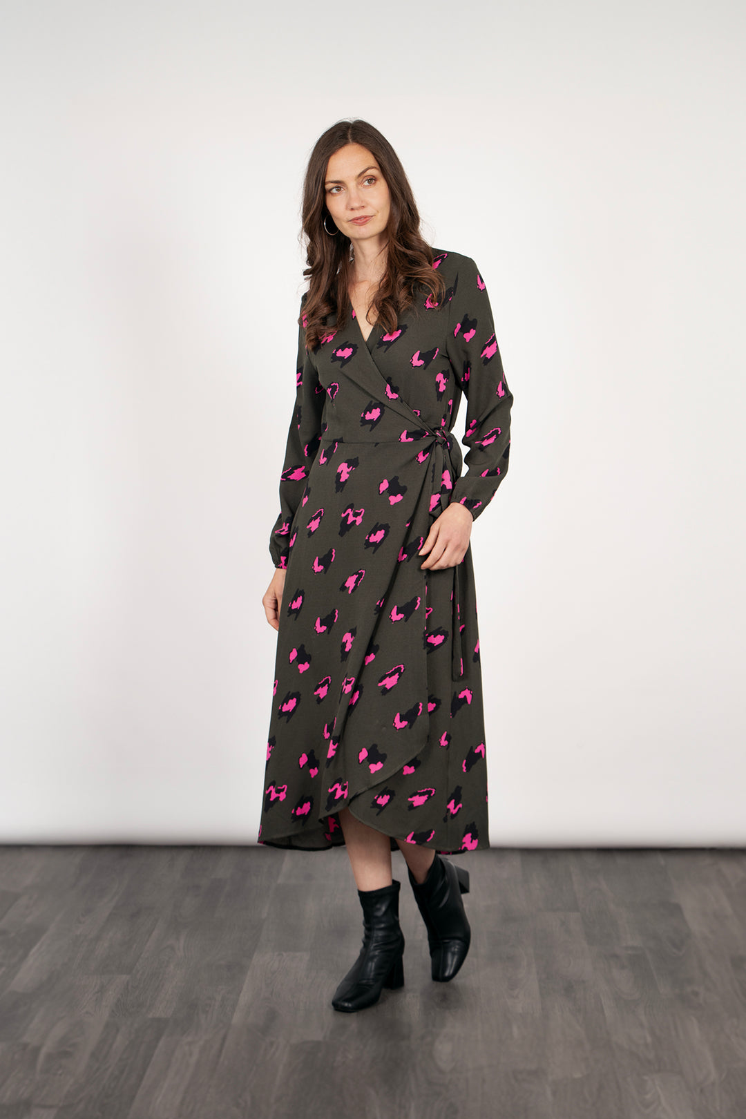 model wearing a long sleeve wrap dress in khaki green with a hot pink leopard print pattern. the dress has a v-neck and waist tie