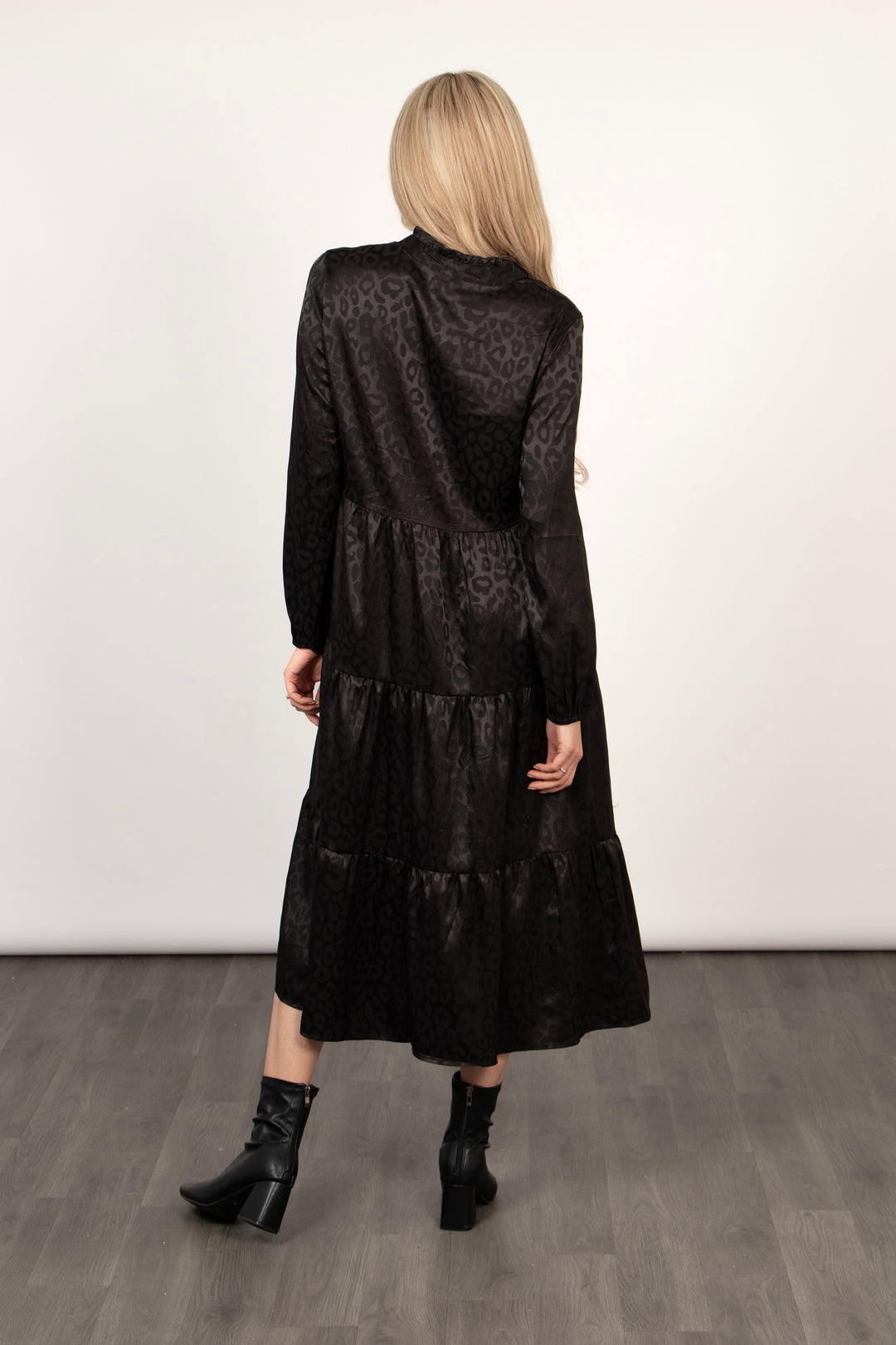 model showing the back of the black leopard print tiered dress. the hemline falls midcalf and the dress is loose fitting