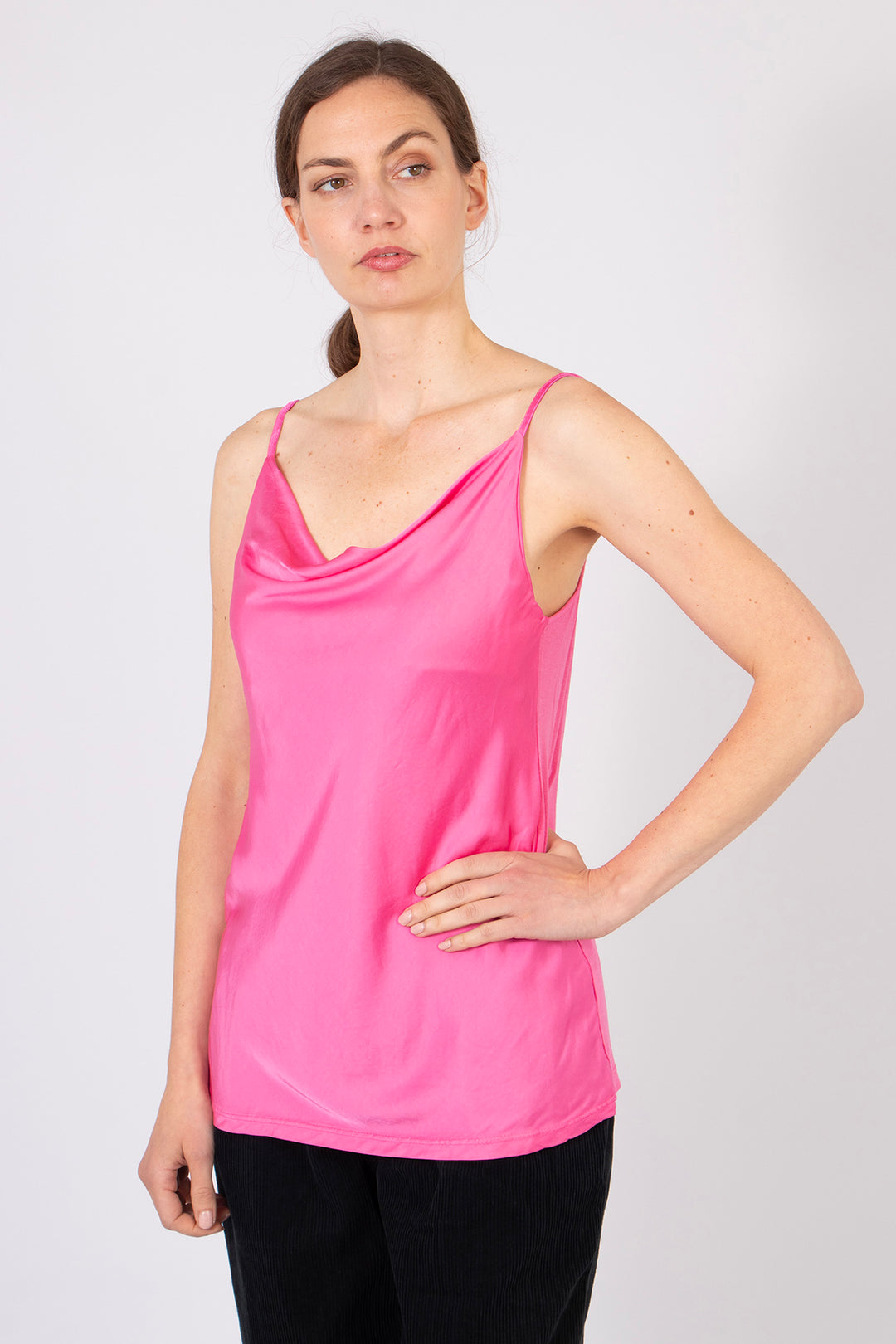 model wearing a light bright pink cowl neck vest top. the top has thin spaghetti straps and falls at the hips.