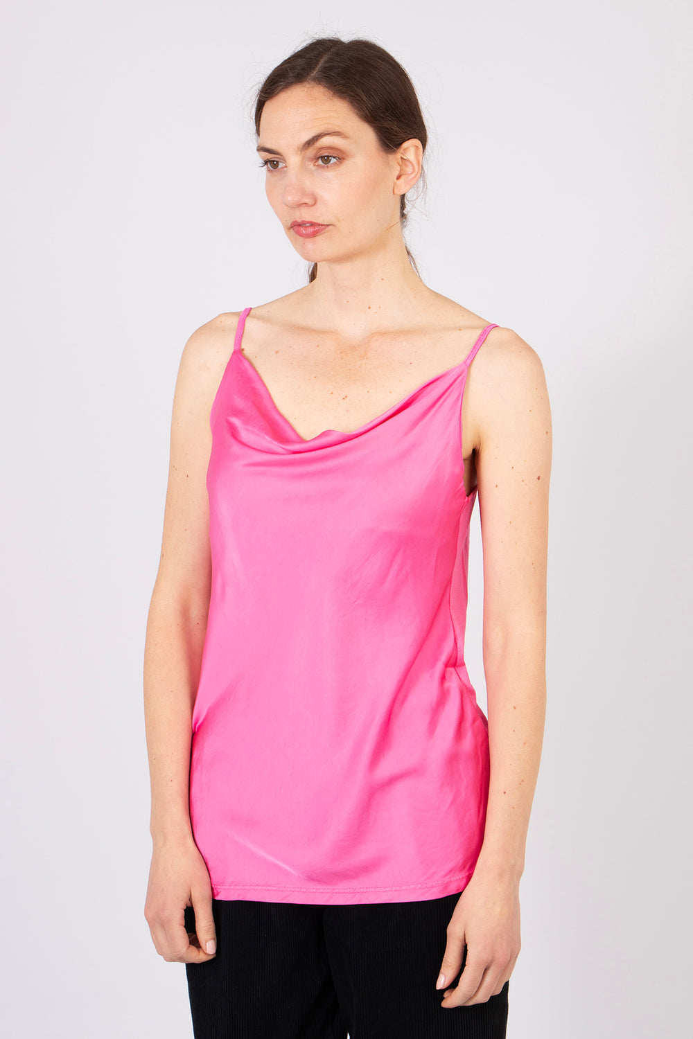 model wearing a plain pink cowl neck vest top paired with black trousers. the vest top is lightweight and has a silky appearance.