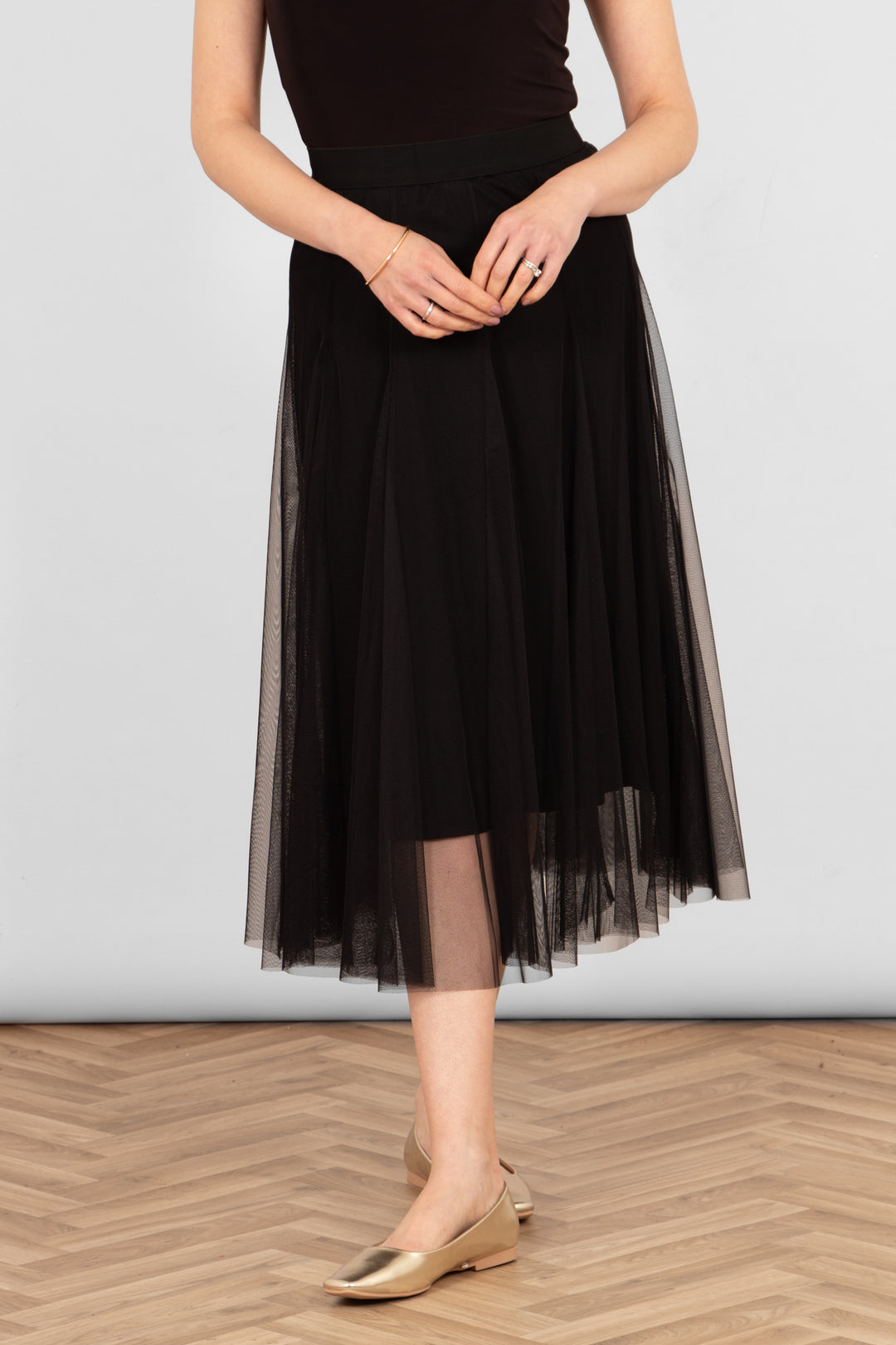 model wearing a midi length plain black tulle skirt with a black underskirt. 