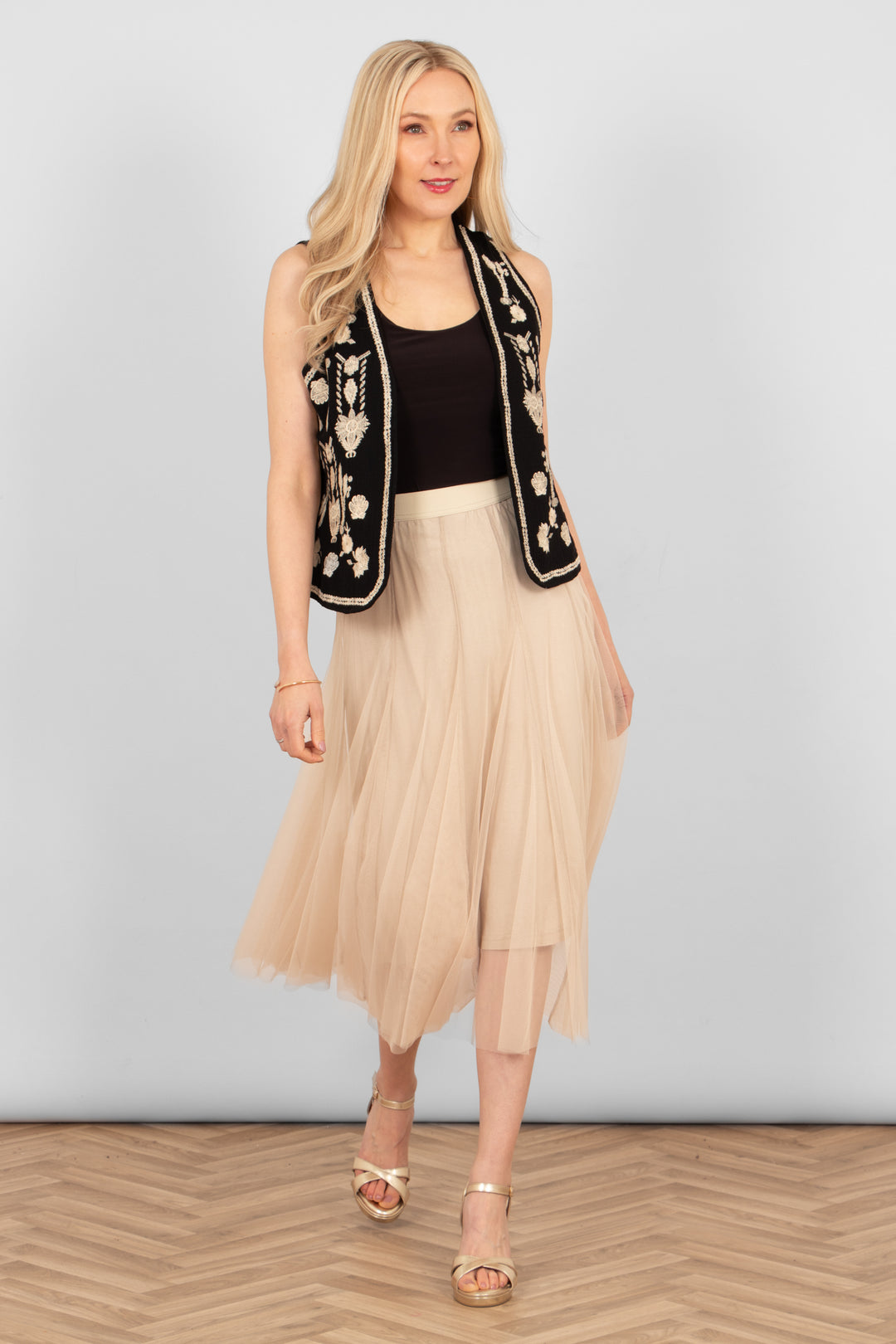 cream tulle midi skirt styled with a plain black vest top, black embroidered floral waistcoat and gold sandals.