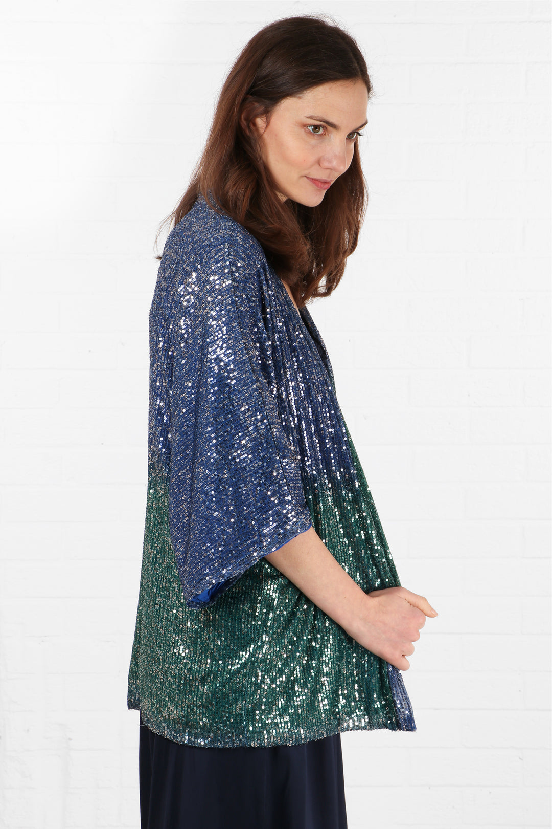 model showing the side view of the kimono jacket, showing all over sequin coverage in blue and green ombre