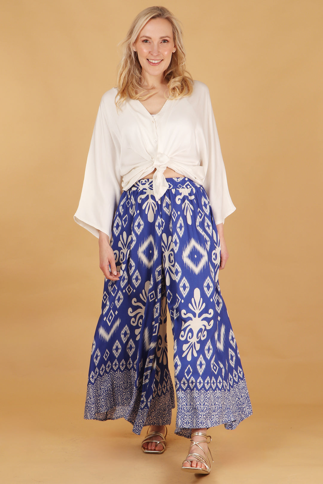 model wearing a pair of blue wide leg palazzo trousers with a white ornate ikat pattern