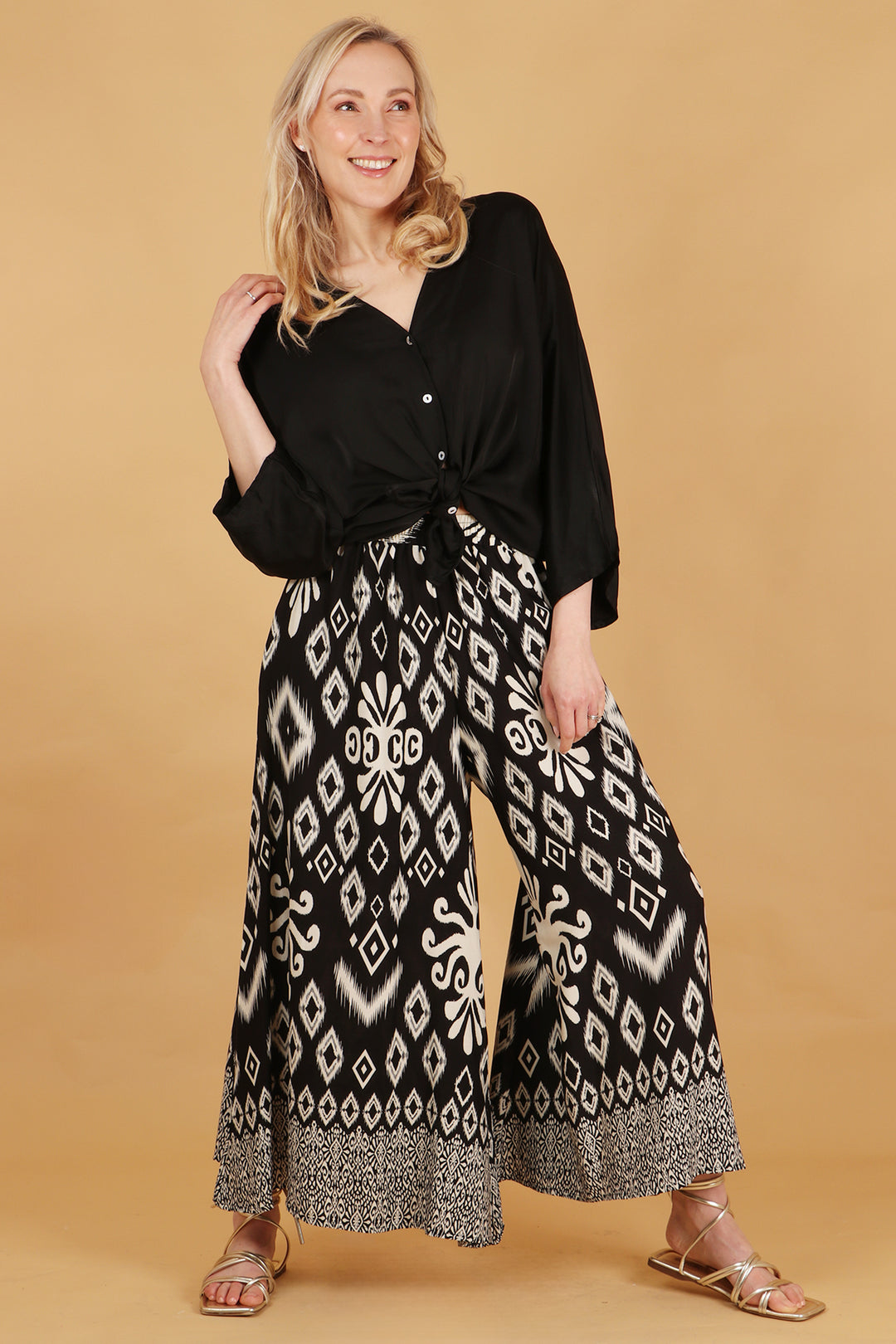 model wearing a pair of loose fitting wide leg palazzo pants in black with a white ornate ikat print 