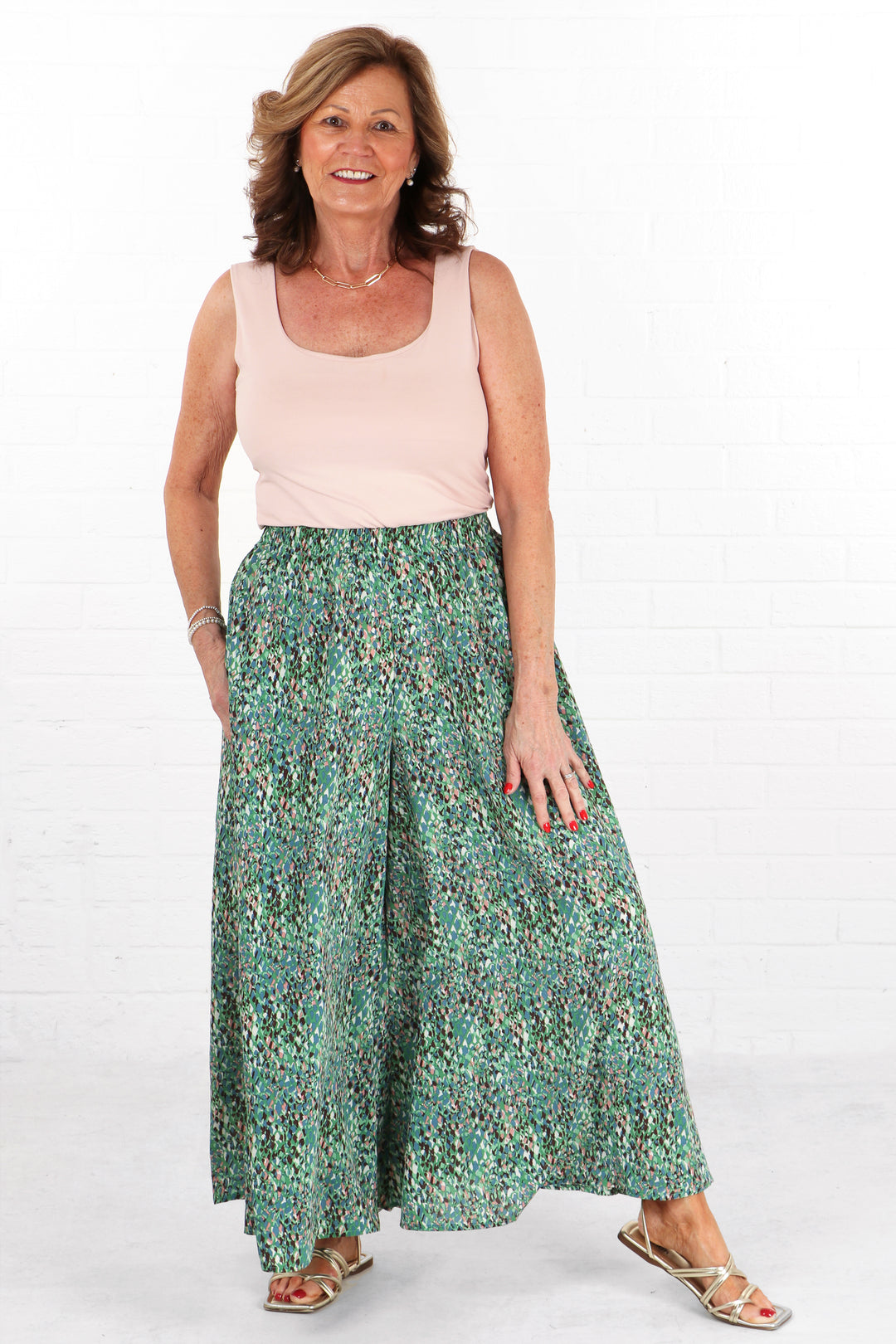 model wearing a pair of long green abstract print palazzo trousers with an elasticated waist and wide leg design