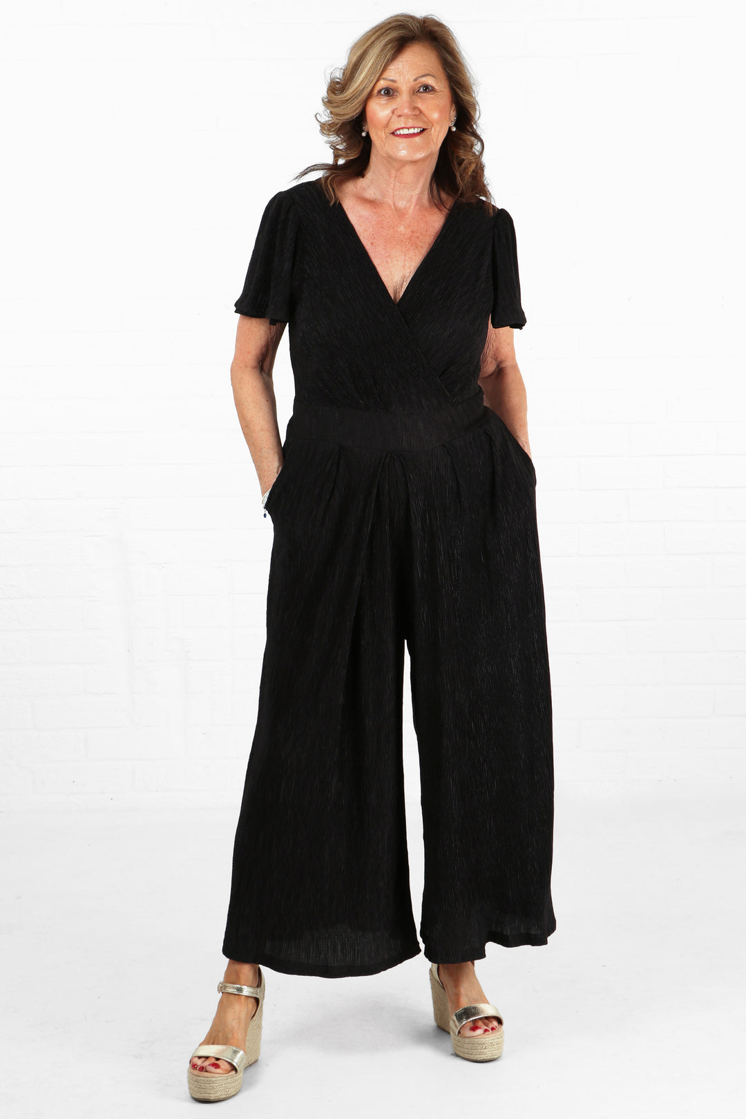 model wearing a black plisse jumpsuit with short angel sleeves and a v neck