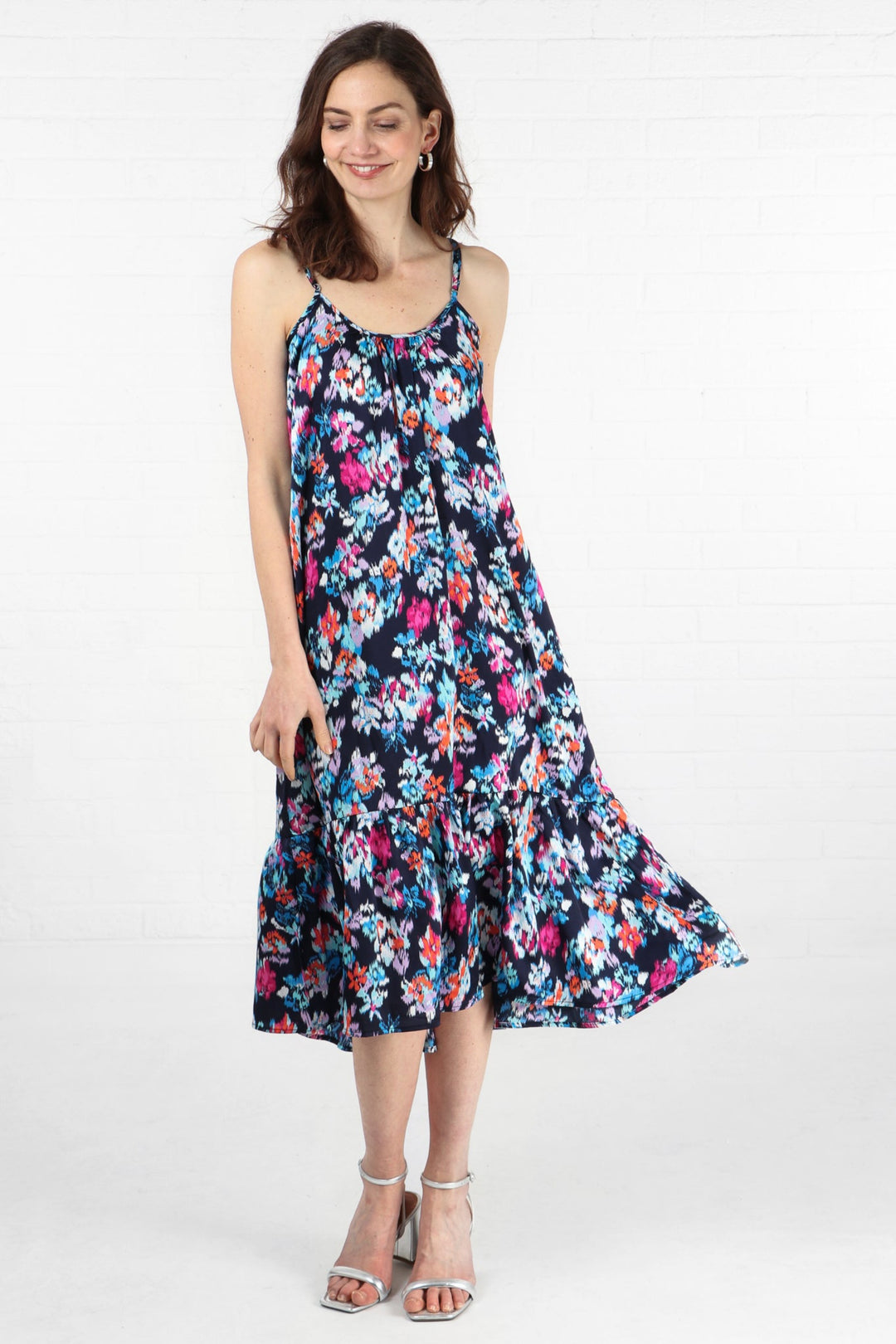 model wearing a navy blue midi length tiered slip dress with spaghetti straps and an all over pink, blue and orange floral print pattern