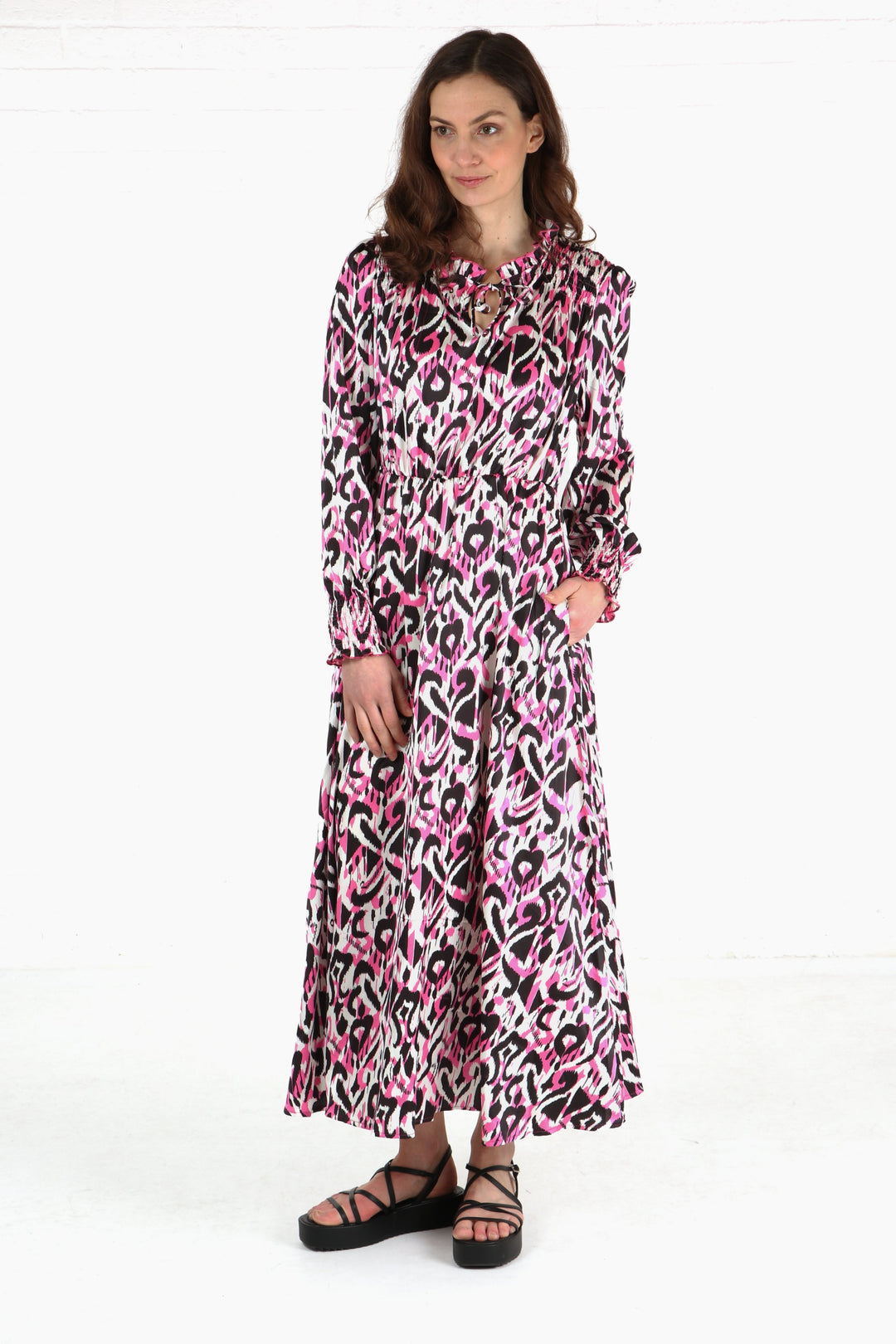 model wearing a long sleeve midi dress in an all over pink and black abstract ikat pattern, the dress has a neck tie  and shirring on the shoulders and cuffs