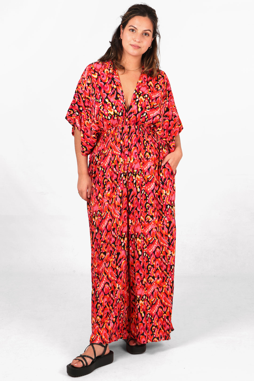 model wearing a pink and black abstract print jumpsuit with full length flared trouser legs, v neck and elbow length angel sleeves