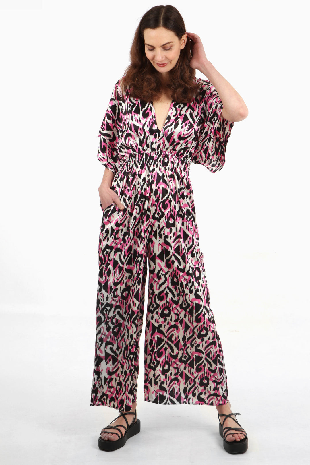 model wearing a pink, black and white abstract ikat pattern jumpsuit with a deep v neck and shirred waist and short elbow length sleeves