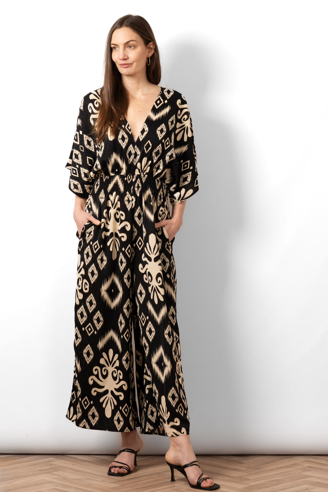 lyra-deep-v-neck-jumpsuit-black-ikat-on-model-styled-with-heeled-sandals-showing-front-pockets