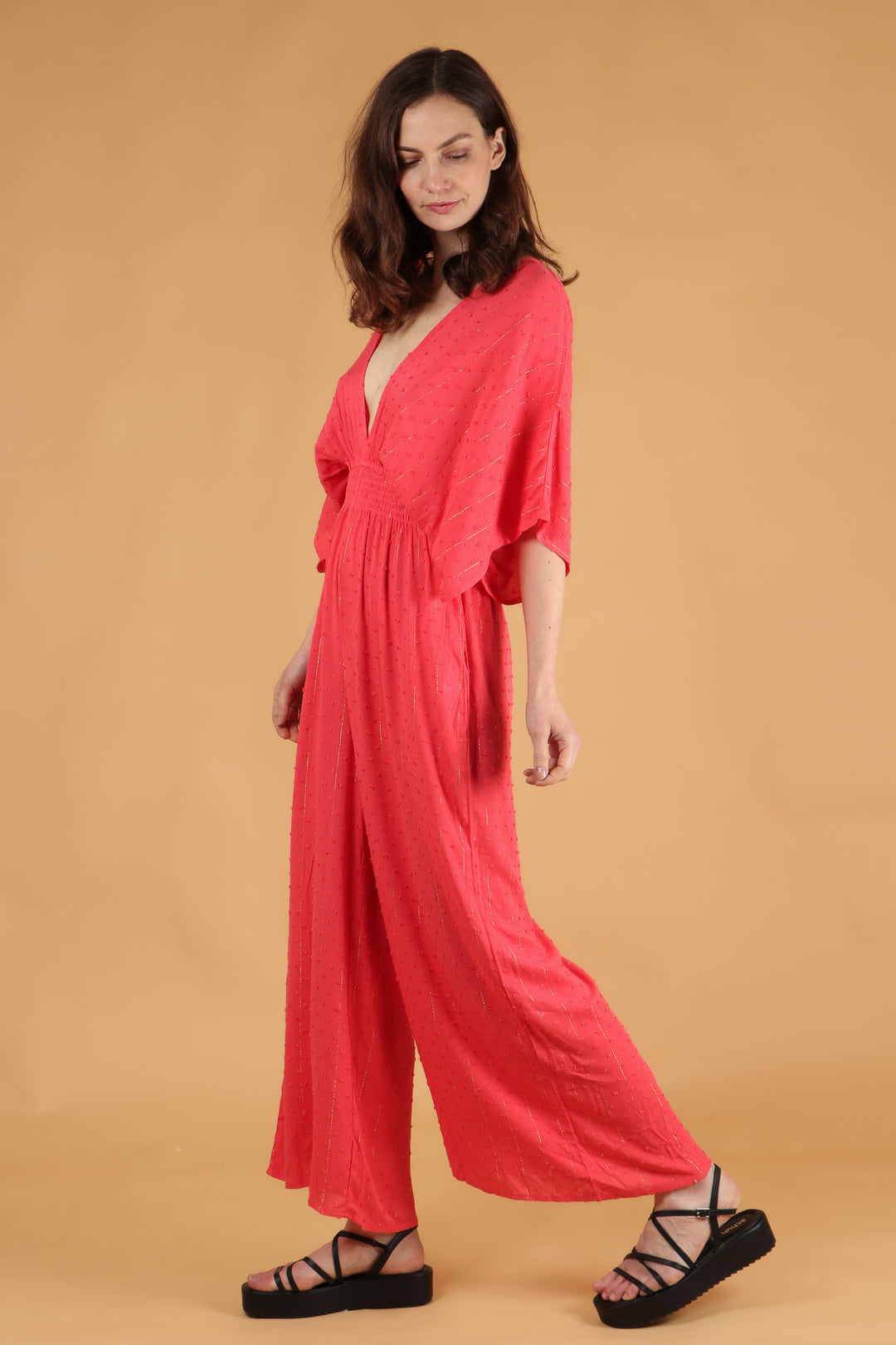model wearing a coral and gold stipe short sleeve flared jumpsuit with a deep v neck