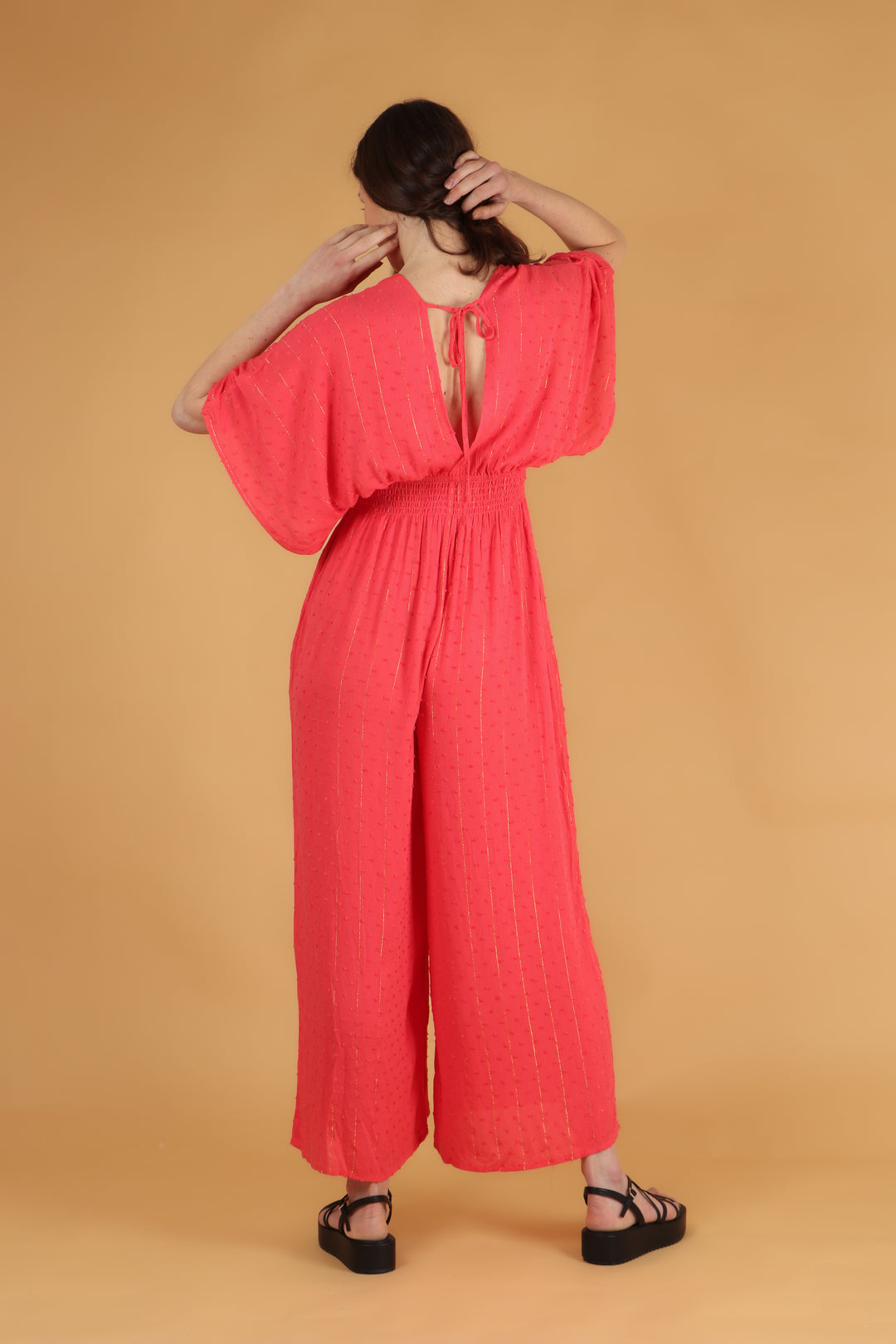model showing the back of the coral jumpsuit showing the shirred elasticated waist and tie at the back of the neck