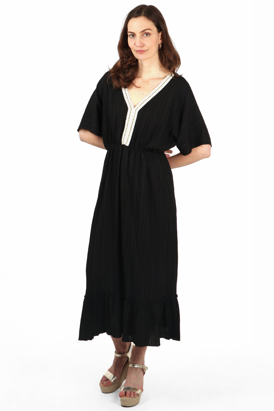 model wearing a midi length 3/4 sleeve black dress with a v neck, there is white and gold robe trim around the v neck