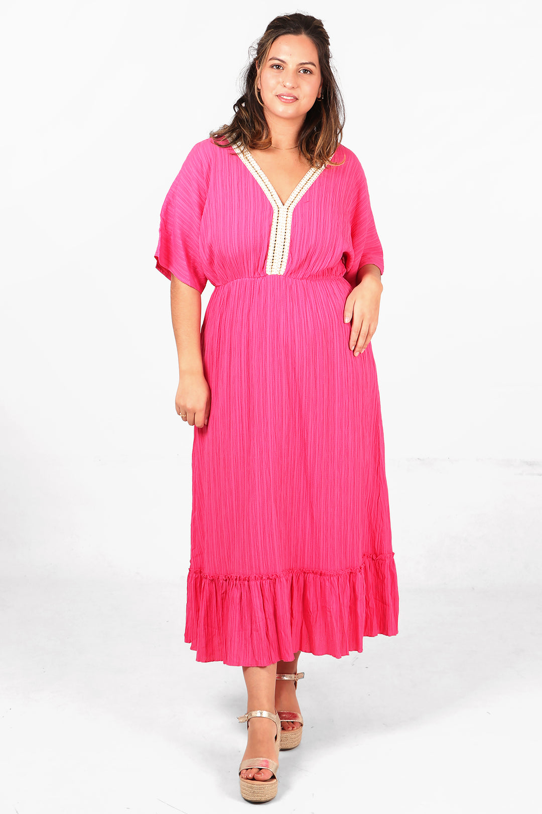 model wearing a midi length 3/4 sleeve pink dress with a v neck, there is white and gold robe trim around the v neck