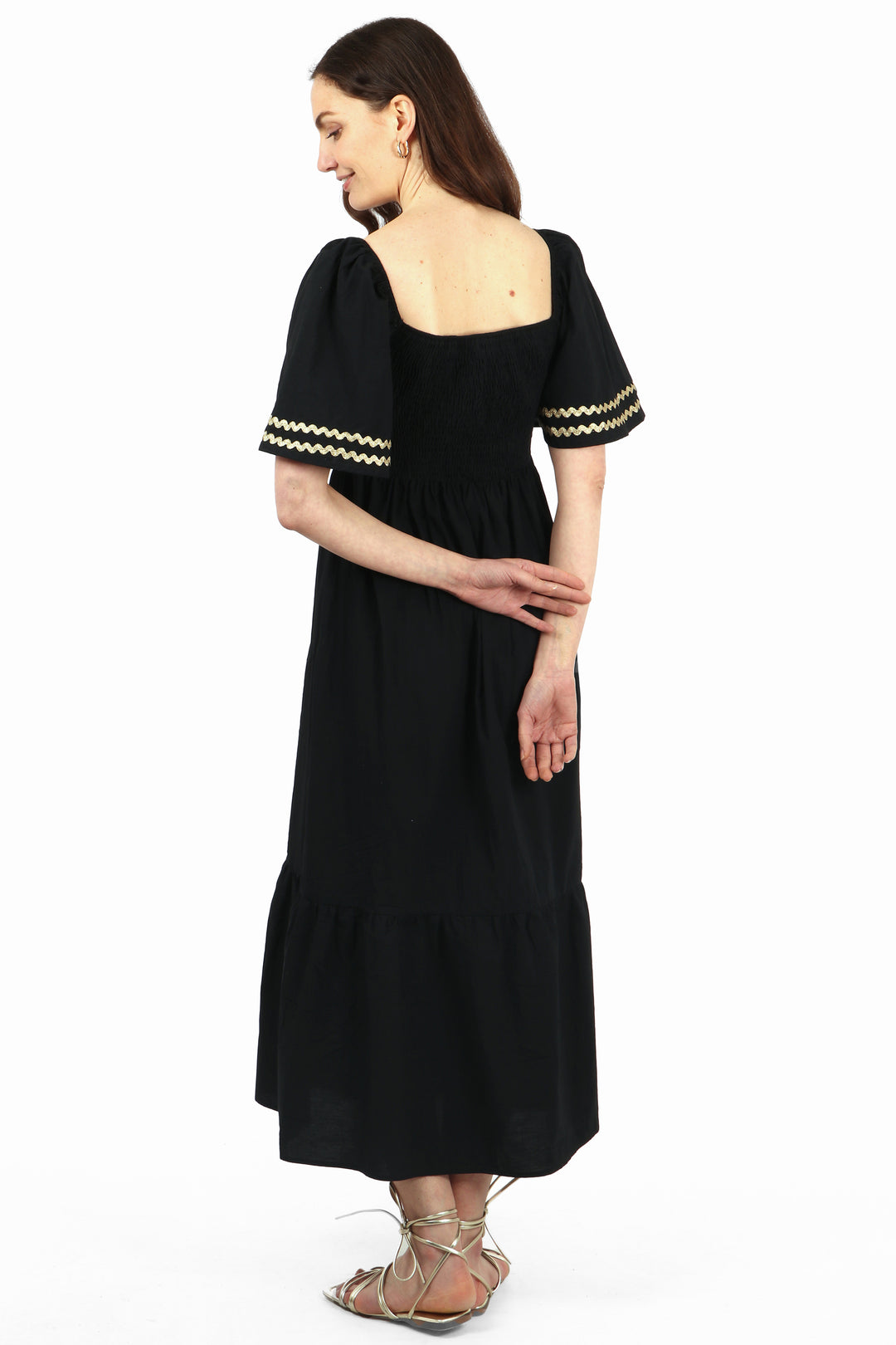 model showing the back of the dress, showing the square neck and gold trim on the sleeves