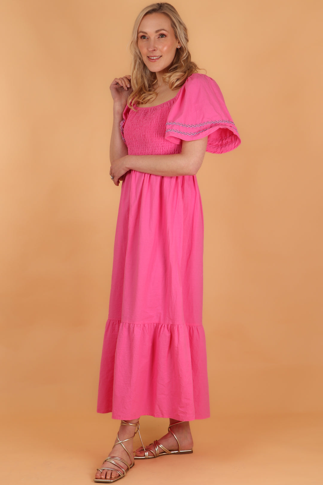 model wearing a long pink tiered hem milkmaid dress with short bell sleeves and square neck